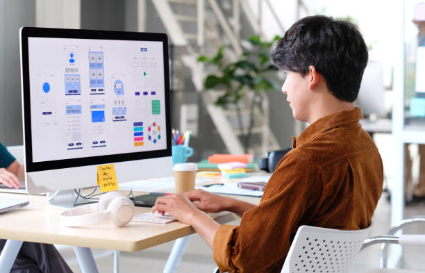 Designer at a desktop computer reviewing app wireframes and a color palette
