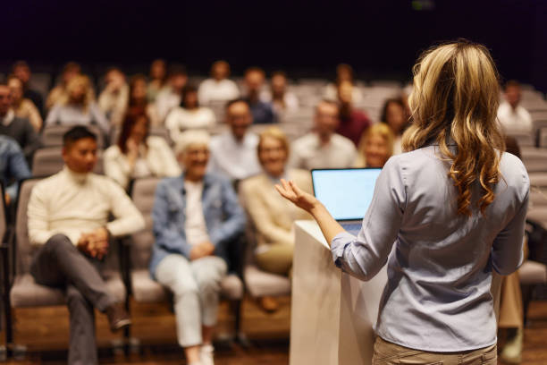 Woman presenting from a podium to a seated auditorium audience