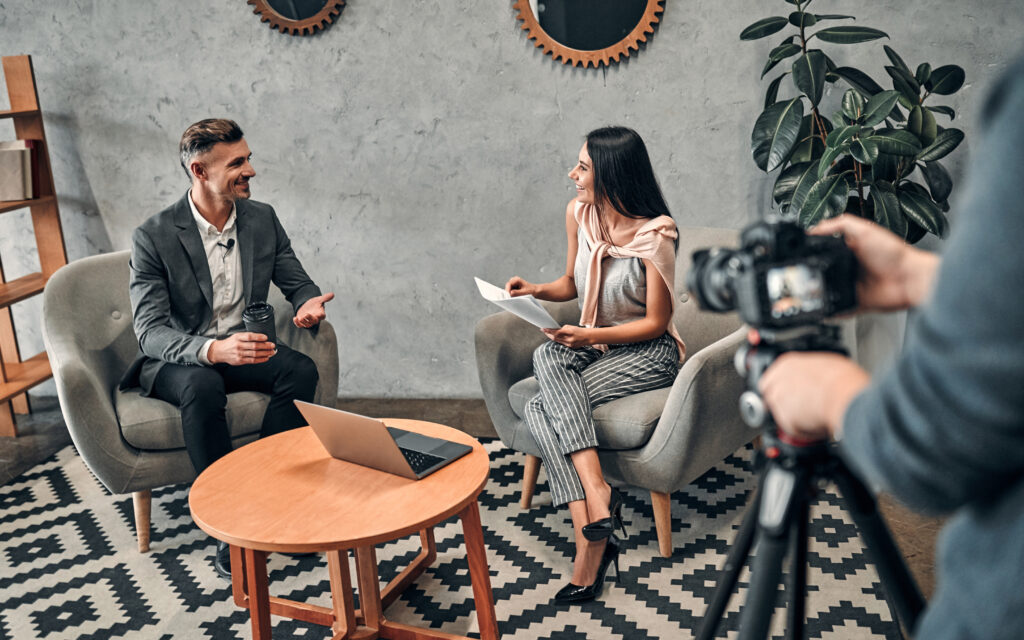 Two people in a mock interview being filmed by a camera operator